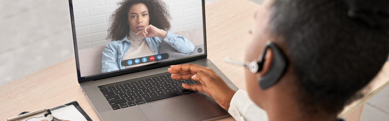 doctor with headset takes notes during telemedicine visit with patient