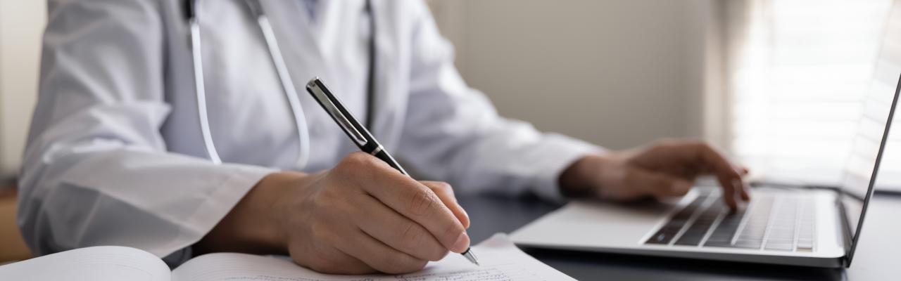 doctor writing notes and using laptop